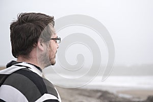 Man in his late twenties looking out towards the sea on a windy day