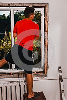 A man in his own house installs a plastic window, installs a new window, a worker uses an electric drill