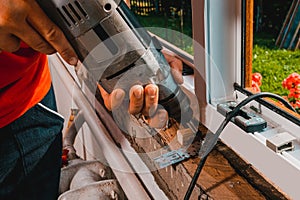 A man in his own house installs a plastic window, installs a new window, a worker uses an electric drill