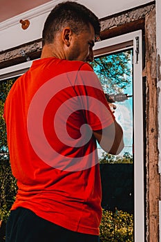 A man in his own house installs a plastic window, installs a new window, a worker uses an electric drill