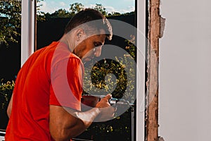 A man in his own house installs a plastic window, installs a new window, a worker uses an electric drill