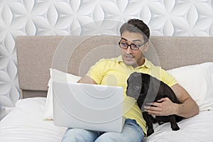 Man and his pet pug working on laptop in the bedroom