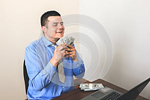 Man with his salary. Office worker holding dollars. Happy face of top manager. Guy in smart shirt and tie at the desk with laptop