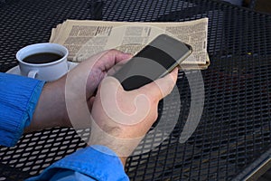 Man with his smartphone at a table with a newspaper and a cup of coffee