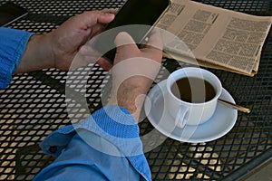 Man with his smartphone at a table with a newspaper and a cup of coffee