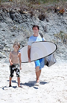 Man and his son arriving at the beach to surf