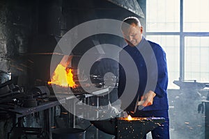 Man hitting molten metal with heavy hammer at forge