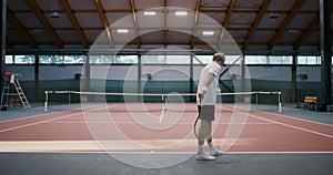 A man hitting tennis ball off floor with a racket and hitting the ball over net