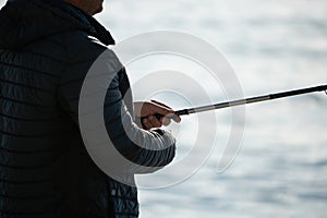 Man hobby fishing on sea tightens a fishing line reel of fish. Calm surface sea. Close-up of a fisherman hands twist