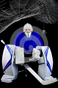 Man in hockey goalie outfit sitting on chair. Above him are cobwebs with a spider. Stay at home concept.