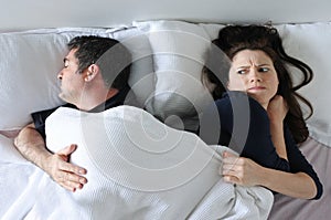 Man hogging the blanket from woman in bed