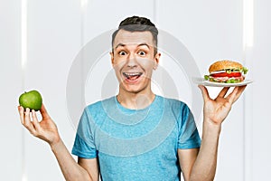 Man hold green apple and a hamburger on light background. Concept of choosing between healthy and unhealthy fast food