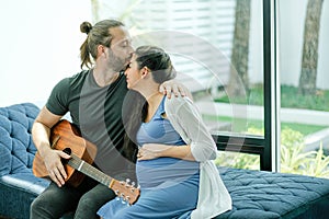 Man hold guitar and kiss on his pregnant wife forehead to express love and care in family. Concept of take care and support lover