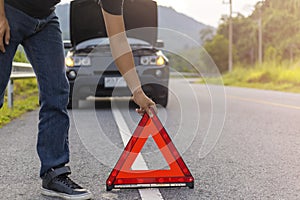 Man hold and put down the red triangle for warning have black color car parking  on road and oper car hood