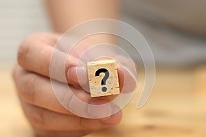 A man hold and shows wooden block with question mark on it, concept of asking question or doubt