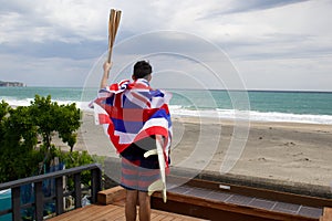 Man hold a torch used in large sporting event , with Hawaiian flag and surfboard.