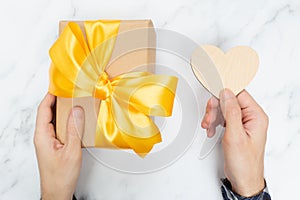 Man holding a beautiful gift box and an empty wooden heart. Marble background. Nice surprise for a birthday or holiday