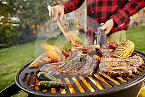 Man holding a beer grilling meat on a BBQ