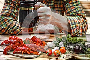 Man holding a beer mug. Boiled red crayfishes on a wooden table.