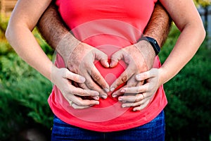 Man holding belly of his pregnant wife making heart. Pregnant woman and loving husband hugging tummy.