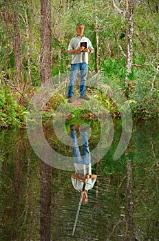 Man holding Bible while his reflection in the water shows him holding a sword representing power of faith
