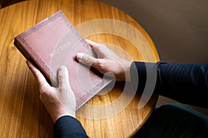 A man is holding and a Bible on the table with atmospheric lighting from the window