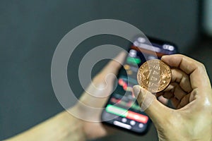 Man holding a bitcoin coin while trading on the other hand