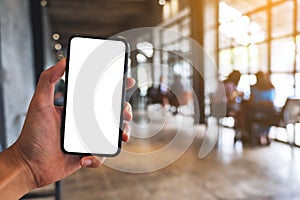 a man holding black mobile phone with blank white screen in cafe