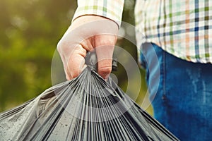 Man holding black plastic bag with trash