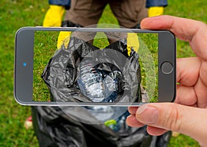 Man holding black plastic trash bag with empty plastic bottles. Photo smartphone.