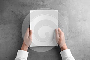 Man holding blank booklet at grey table. Mock up for design