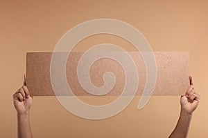 Man holding blank cardboard banner on beige background, closeup. Space for text