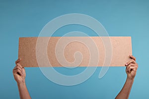 Man holding blank cardboard banner on light blue background, closeup. Space for text