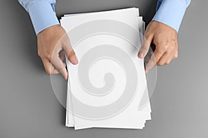 Man holding blank paper sheets for brochure at grey table, top view.