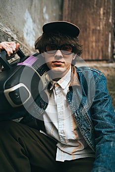 Man holding boombox on his shoulder sitting on stairs. 90s retro style nostalgia concept