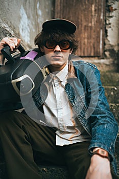 Man holding boombox on his shoulder sitting on stairs. 90s retro style nostalgia concept