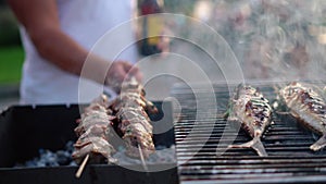 Man holding bottle upturn spit with pork meat. Smoke rising from grilled fish