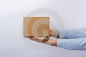 Man holding box at arm`s length. White background. Square cardboard box. Delivery of parcels. Side view