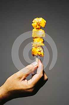 Man holding a brochette of fried potatoes with melted cheese