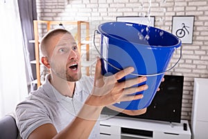 Man Holding Bucket While Water Droplets Leak From Ceiling