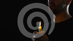 Man holding candle and praying against dark background, confession to God