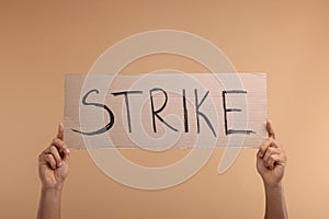 Man holding cardboard banner with word Strike on beige background, closeup