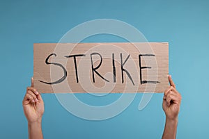 Man holding cardboard banner with word Strike on light blue background, closeup