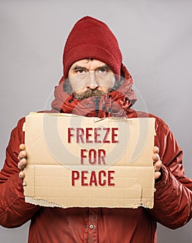 Man holding cardboard sign with Freeze for Peace text in winter coat freezing in the cold