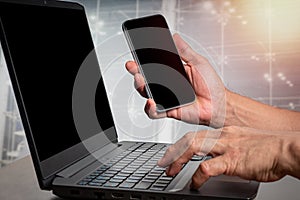 Man holding a cell phone with his right hand (focus), a labtop computer on the table