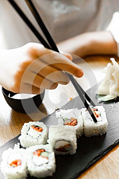 Man holding a chopstick with Salmon roll on restaurant table. Asian man eating salmon roll set in Asian restaurant.