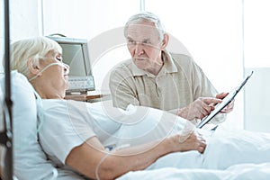 Man holding clipboard and looking at sick wife in clinic