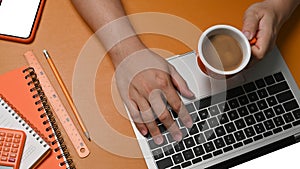 Man holding coffee cup and using laptop computer on brown leather.