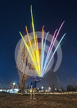 A man is holding a colorful fireworks in the night registering the motion of the light