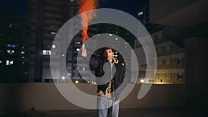 Man holding colorful flare at night cityscape framing urgent signal. Latino guy